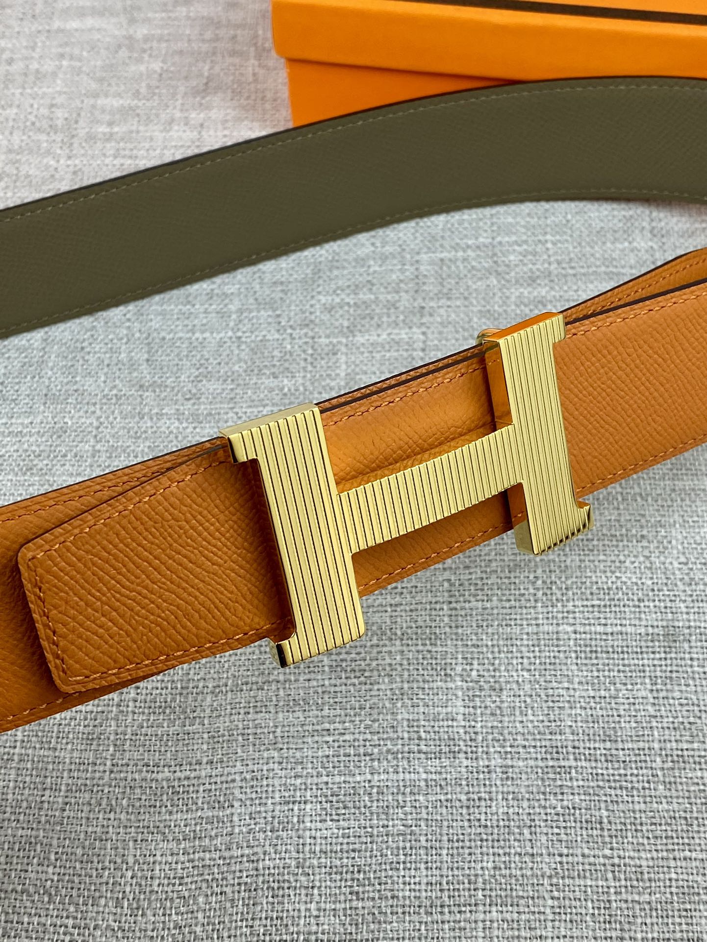 Orange leather belt with ribbed H buckle in light gold tone, close-up