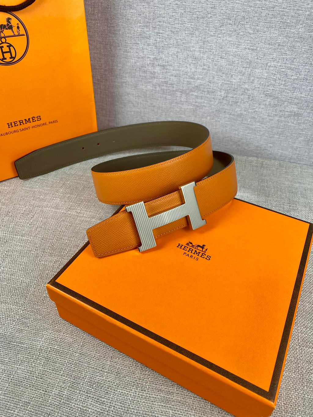 Two-tone leather belt with orange strap, olive underside, and centered H buckle