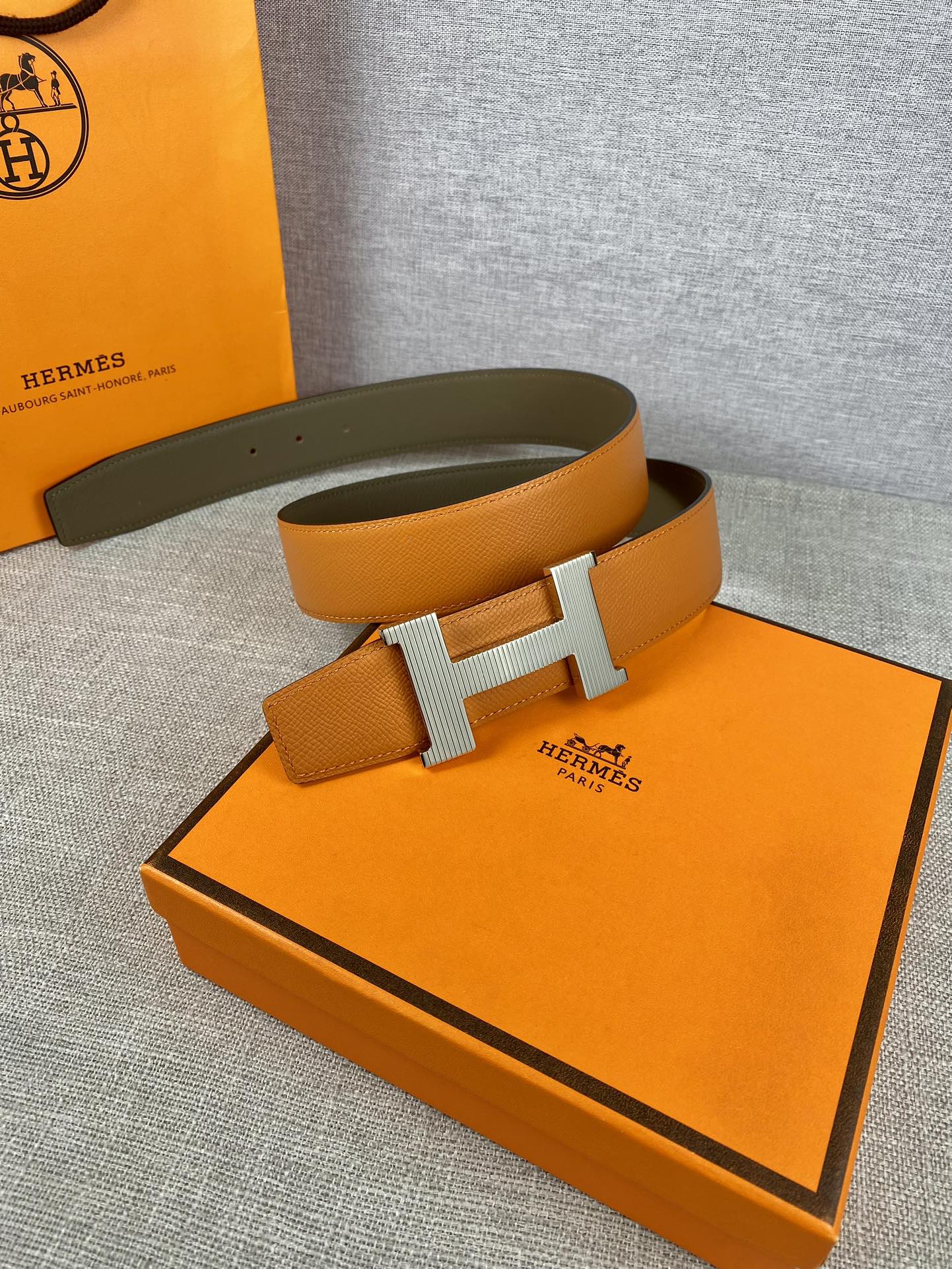 Two-tone leather belt with orange strap, olive underside, and centered H buckle