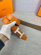 Two-tone leather belt with orange strap and white-gloved hand, H buckle close-up
