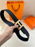 Dark leather belt with metallic H buckle, held in a hand