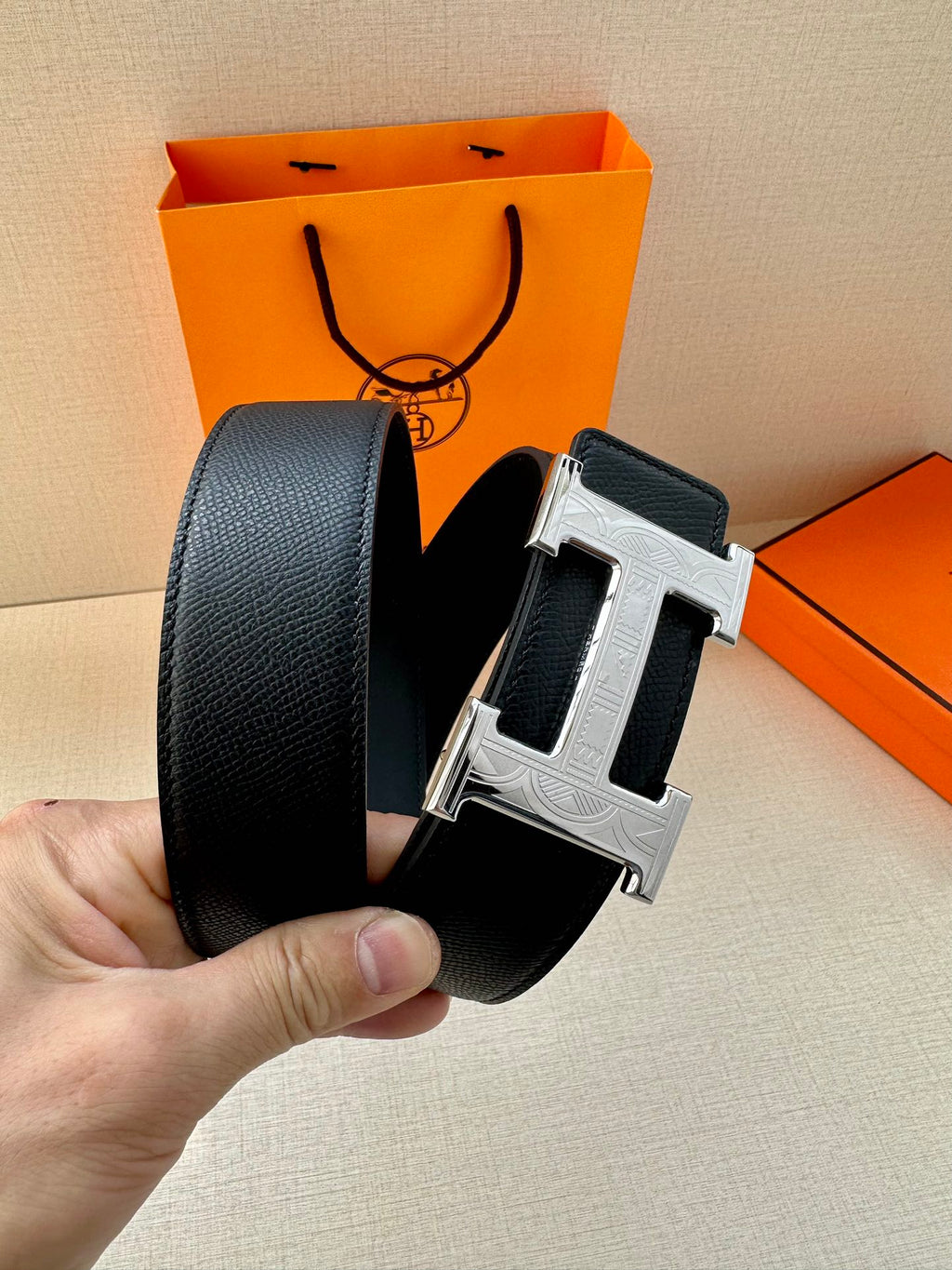 Dark leather belt with silver-tone H buckle, close-up on clasp