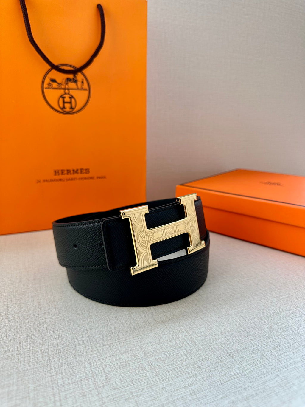 Dark leather belt with metallic H buckle, resting on display surface