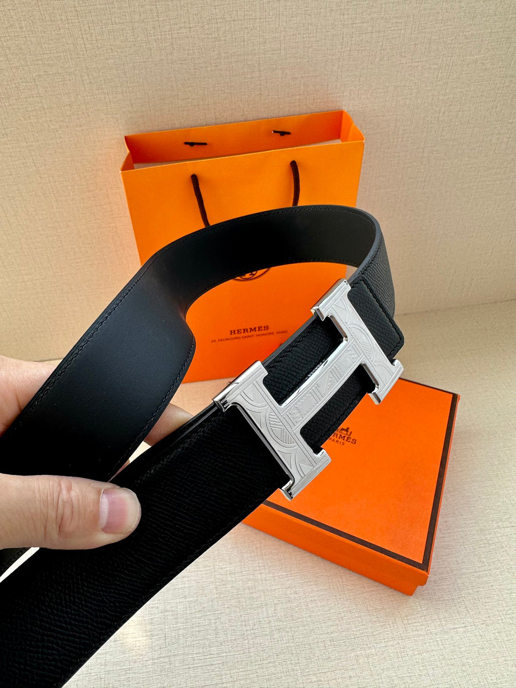 Dark leather belt with large metallic H buckle on textured strap