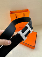 Dark leather belt with large metallic H buckle on textured strap