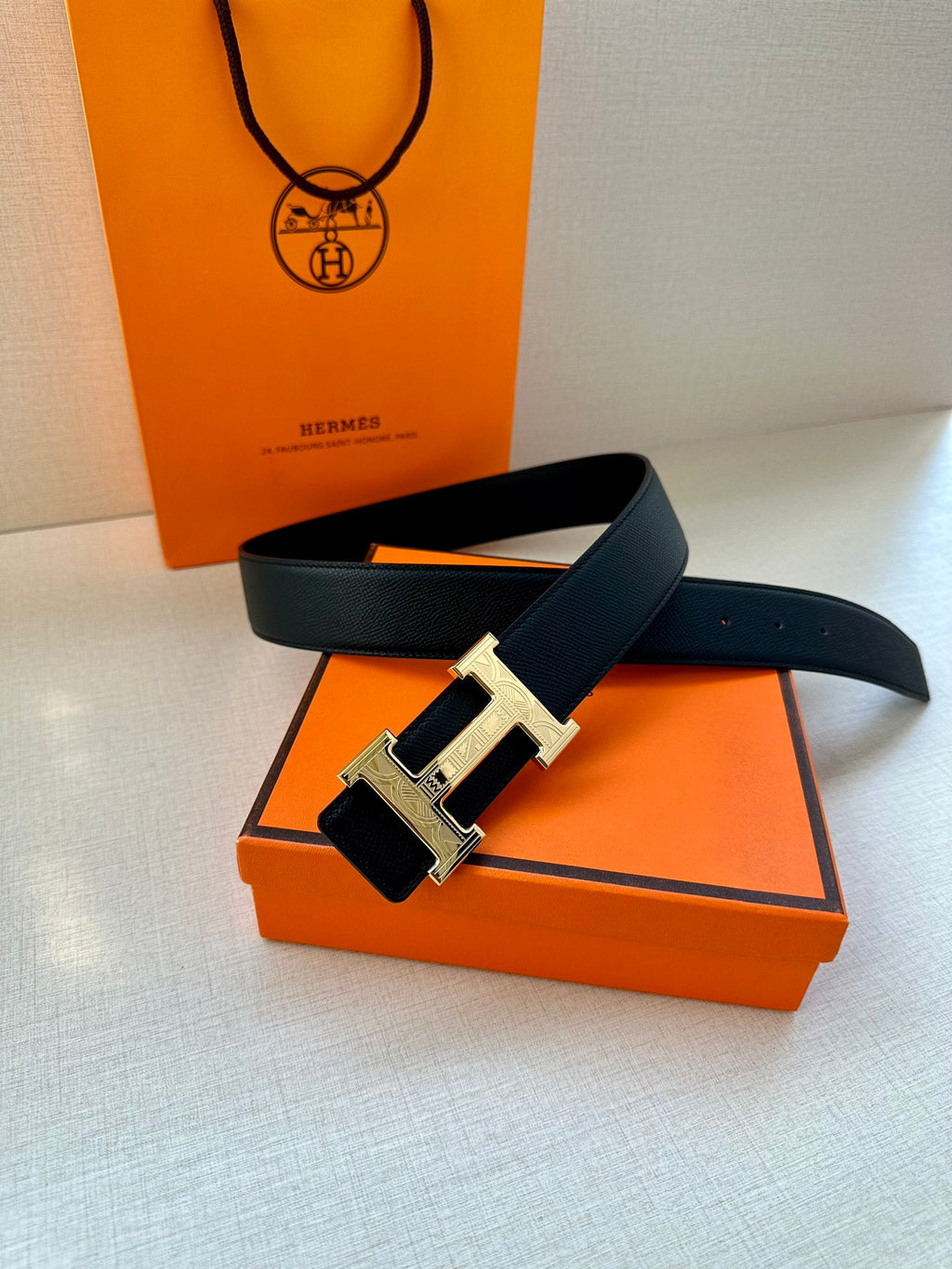 Dark leather belt with metallic H buckle, laid across an orange box