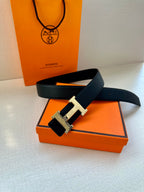 Dark leather belt with metallic H buckle, laid across an orange box