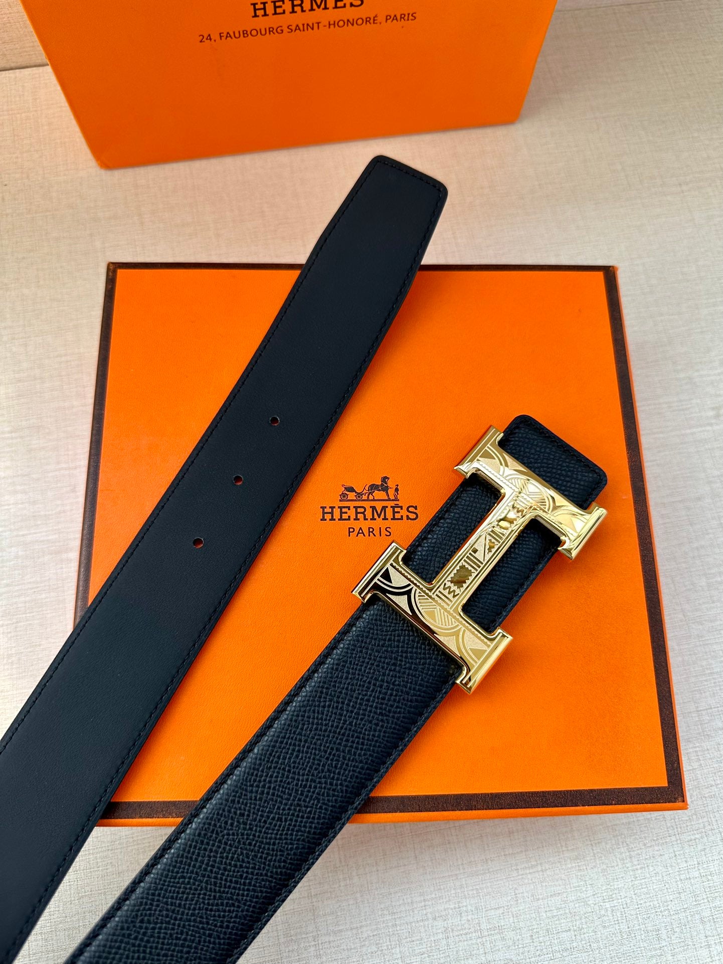 Dark leather belt with metallic H buckle, close-up on strap and clasp