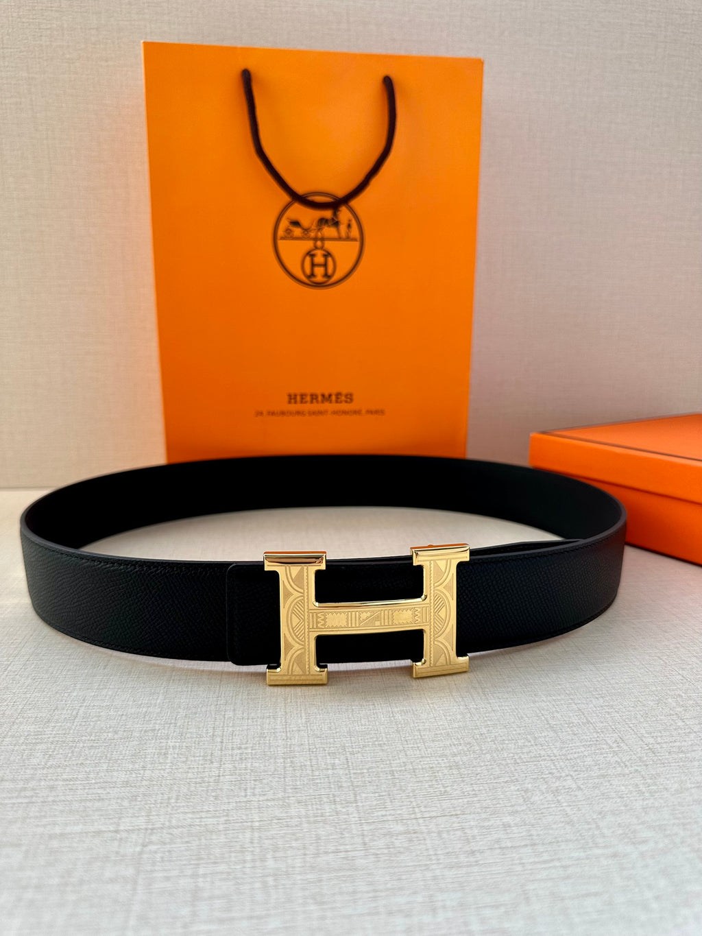 Dark leather belt with wide metallic H buckle, belt lying flat