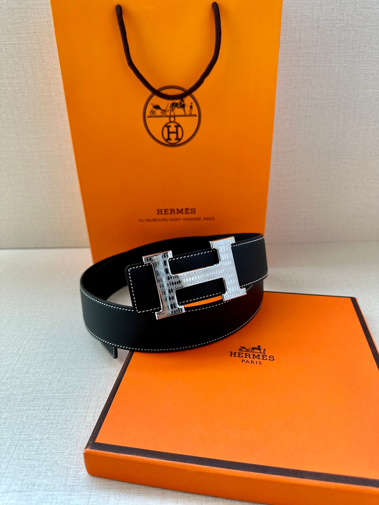 Hermes leather belt with silver-and-gold H buckle, centered closure, belt holes visible