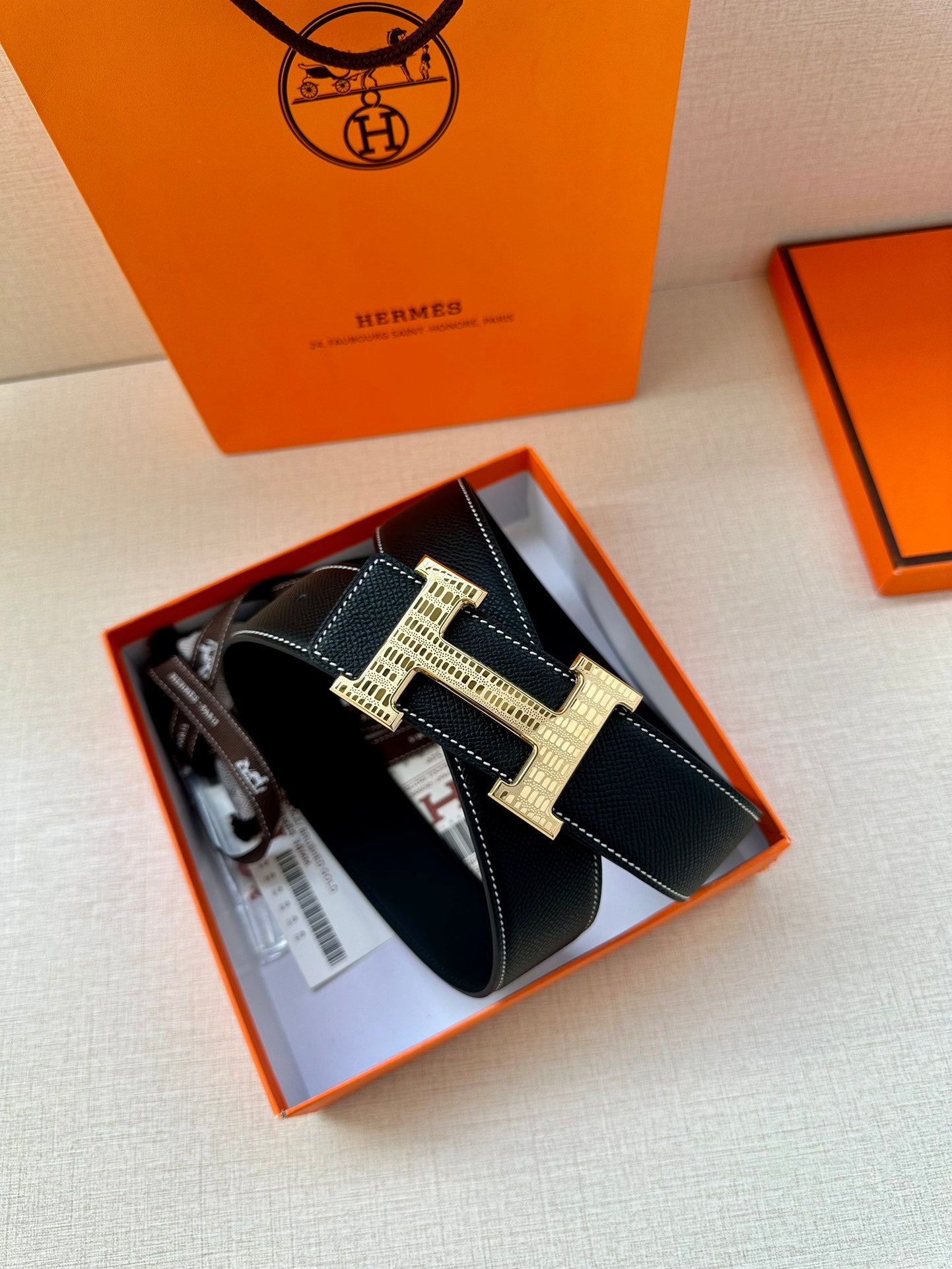Hermes leather belt with H buckle in silver and gold, shown inside its box packaging