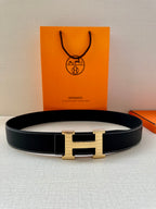 Hermes leather belt with centered H buckle in silver and gold, lying flat with visible holes