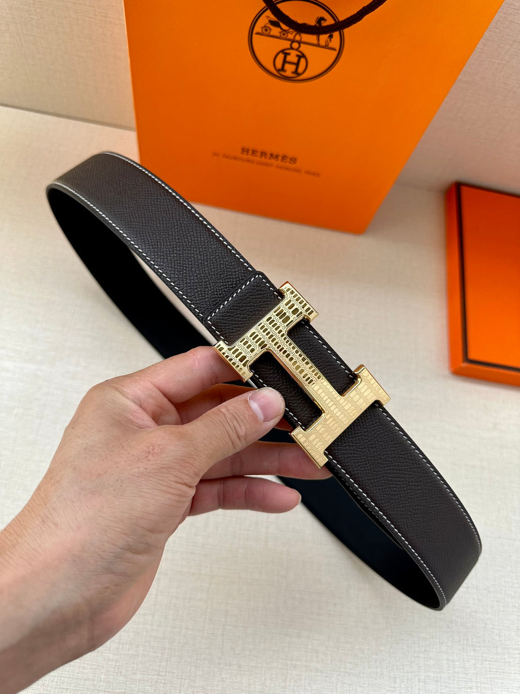 Dark leather belt with gold-tone H-style buckle and textured strap detail