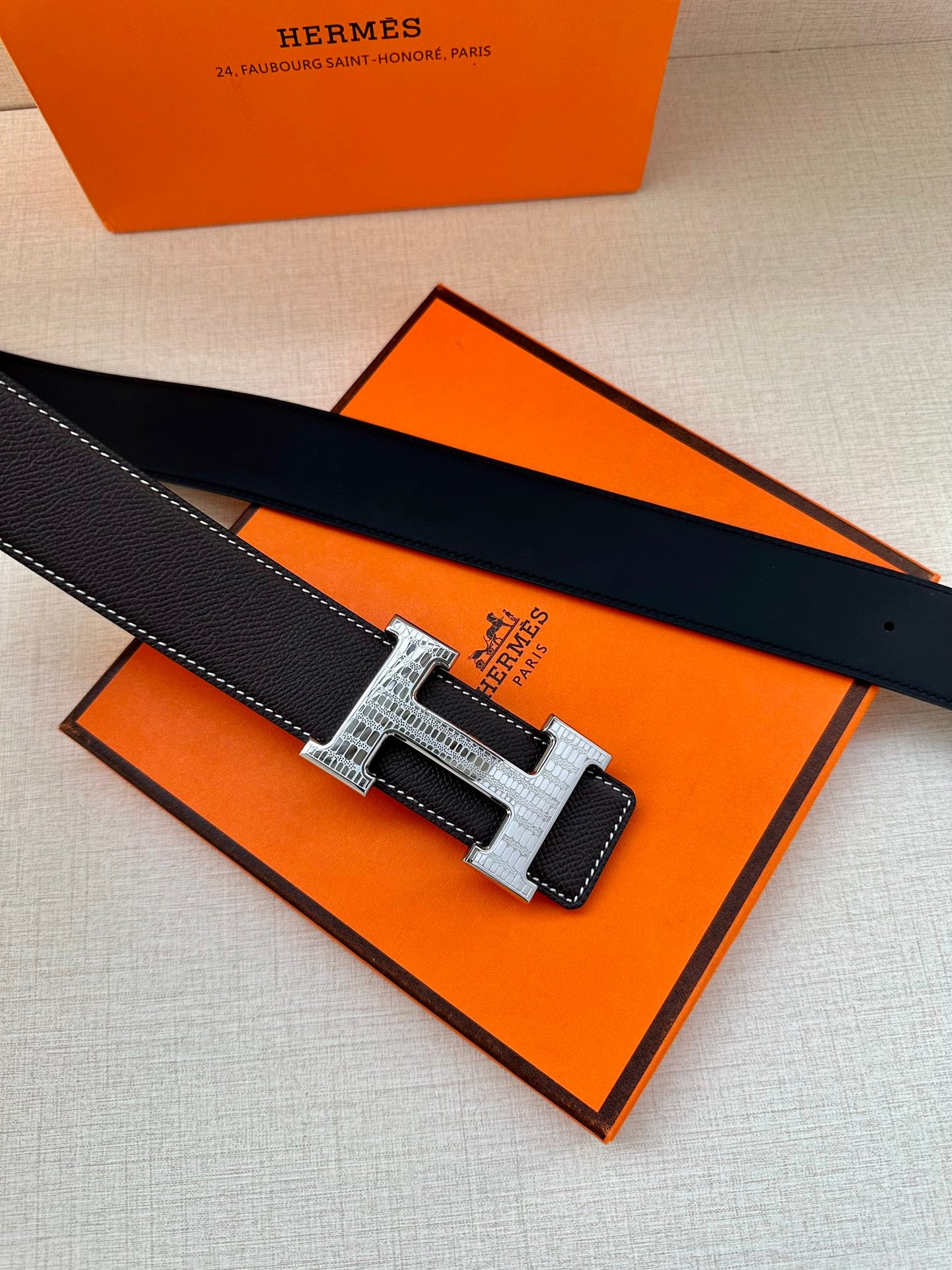 Dark leather belt with silver-tone buckle laid on an orange gift box