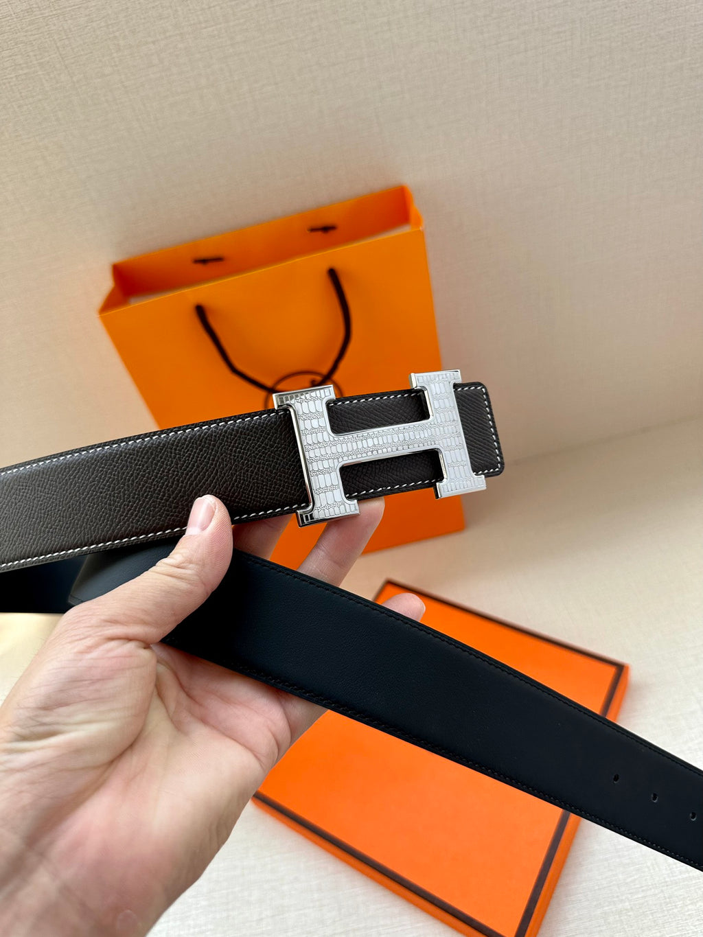Dark leather belt close-up with silver-tone buckle and hand holding