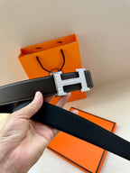 Dark leather belt close-up with silver-tone buckle and hand holding