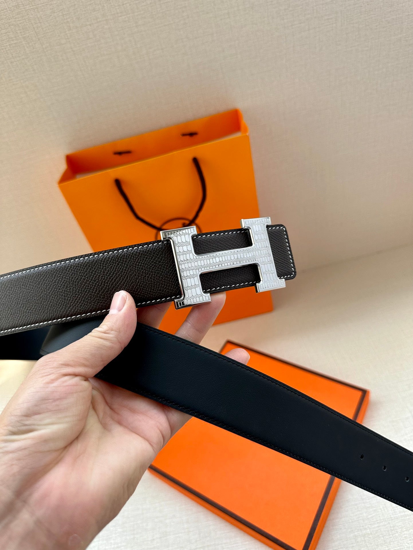Dark leather belt close-up with silver-tone buckle and hand holding