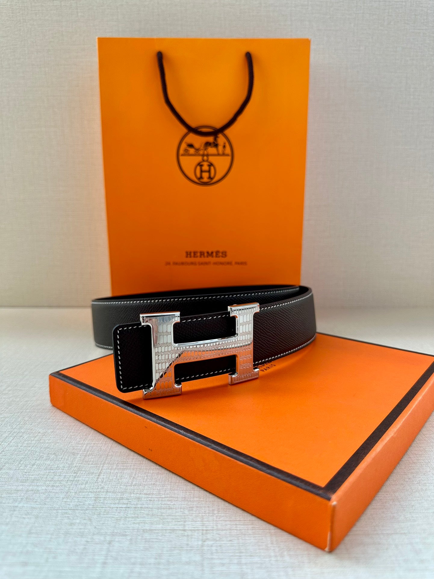 Dark leather belt with silver-tone buckle on an orange box