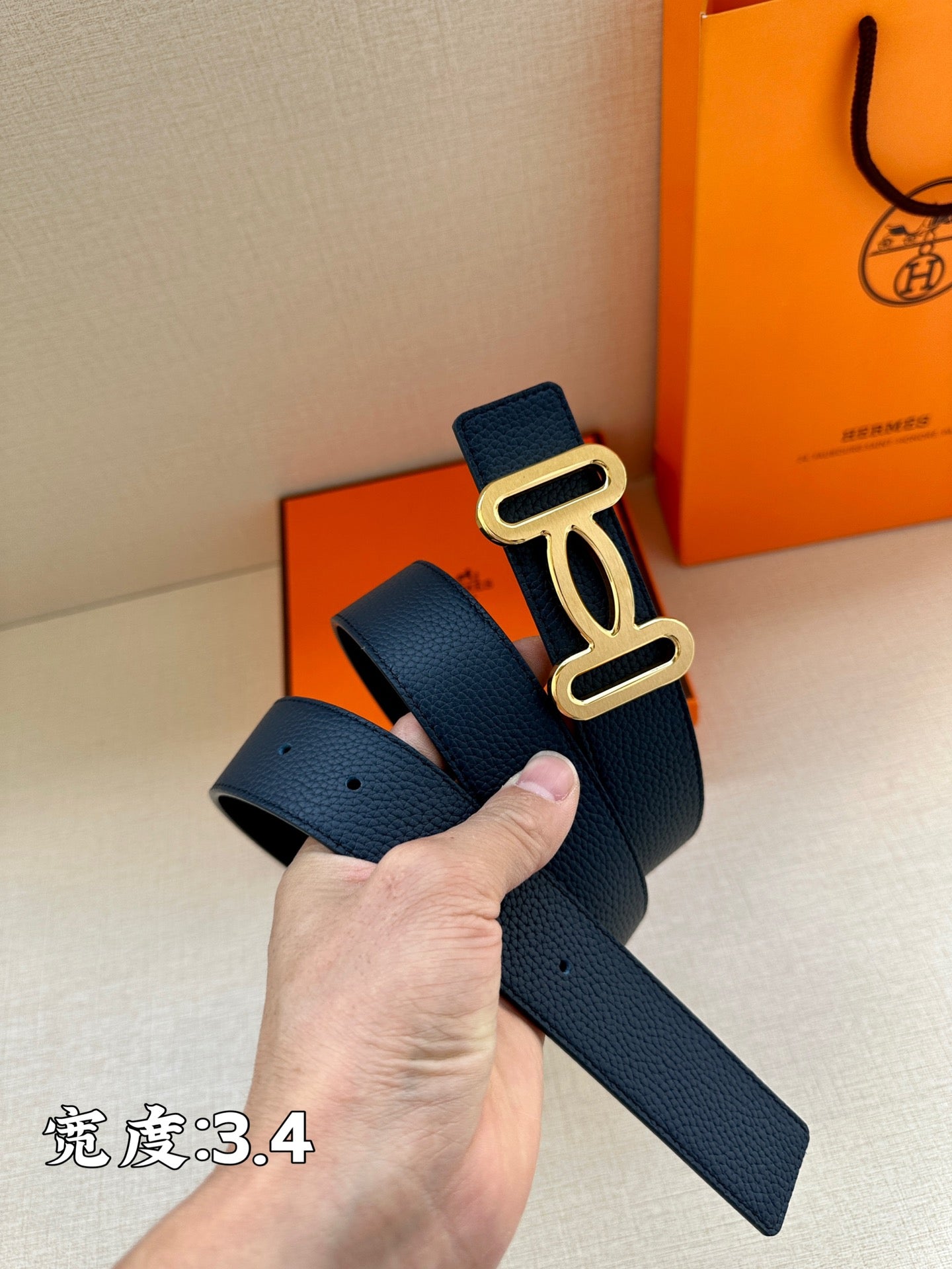 Navy leather belt with gold-tone double buckle, hand holding