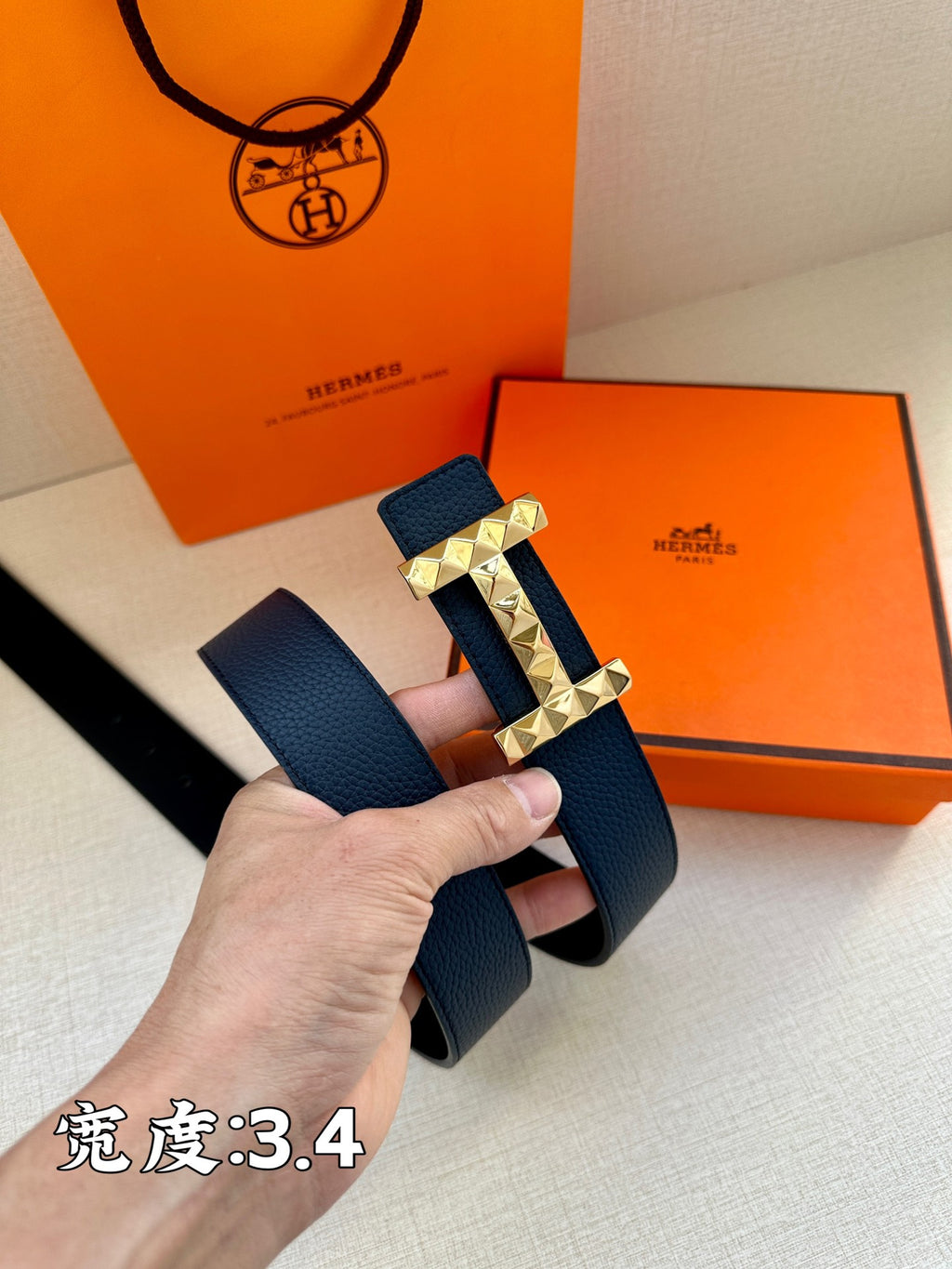 Hermes leather belt, dark blue strap with gold-toned studded buckle, angled view