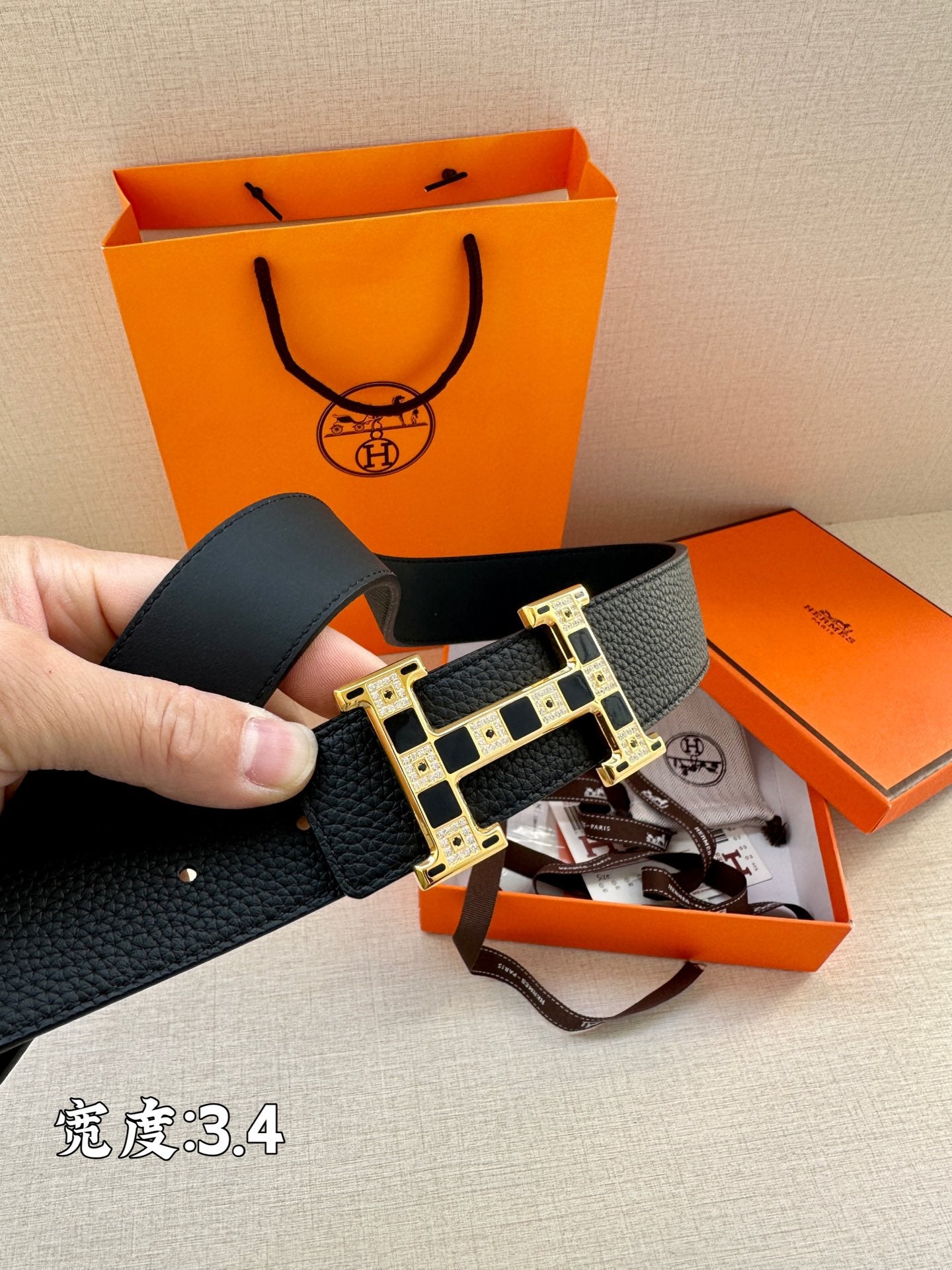 Dark leather belt with gold-tone rectangular buckle and signature-style geometric inlay.