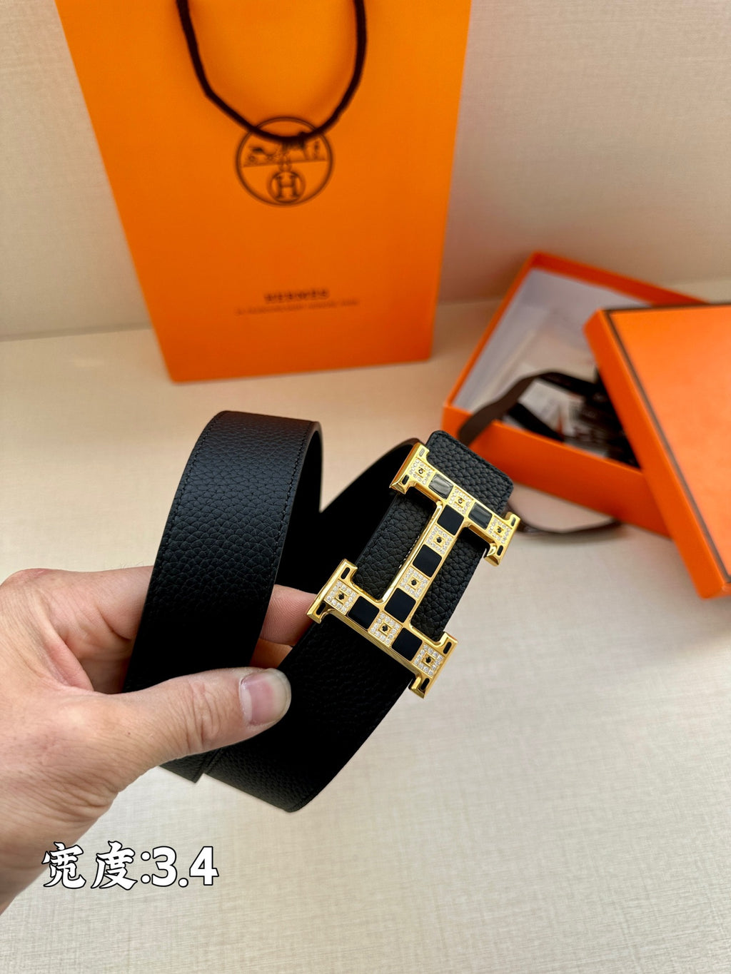 Dark leather belt with gold-tone buckle and textured finish, held in hand.