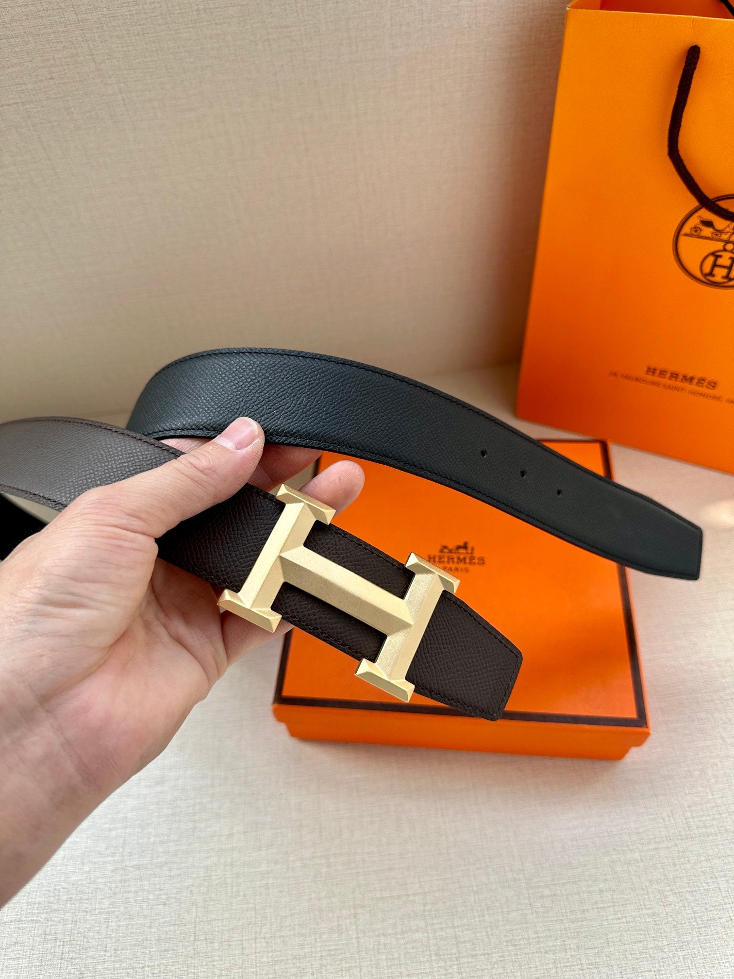 Leather belt close-up: dark pebbled strap with gold-tone H buckle