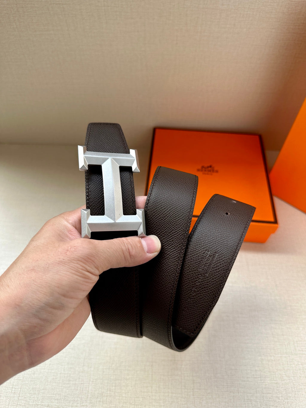 Leather belt with dark pebbled strap and silver-tone H buckle, held up