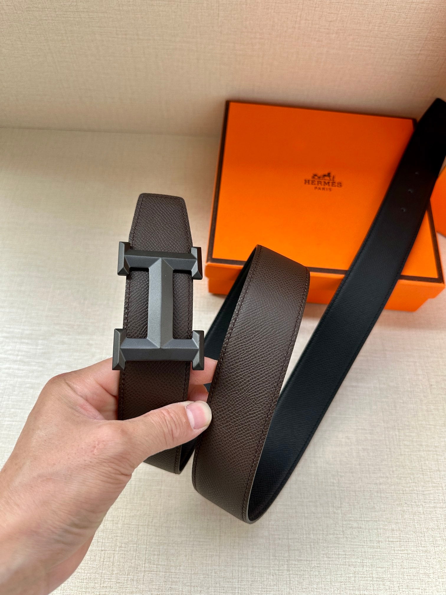 Leather belt with dark pebbled strap and dark metal H buckle, held up