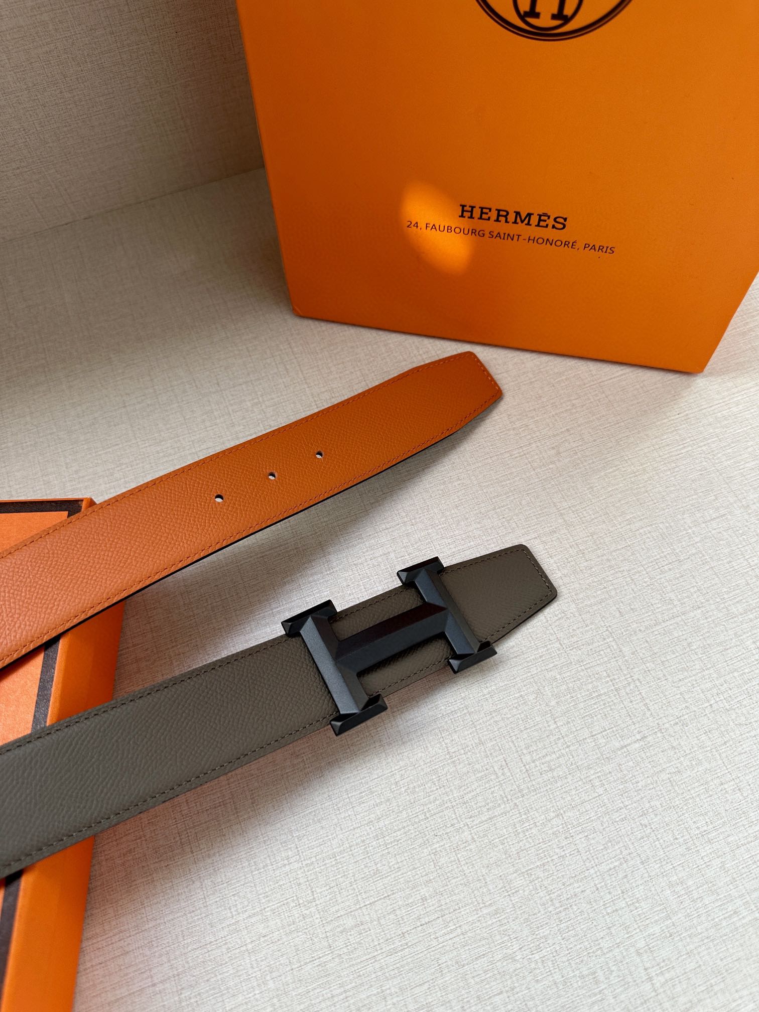 Hermes belt with gray strap and silver buckle detail, plus orange strap end