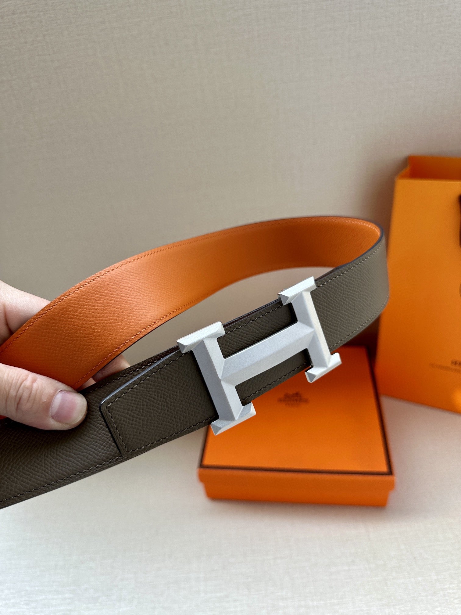 Hermes belt with dark gray strap, orange lining, and silver buckle detail