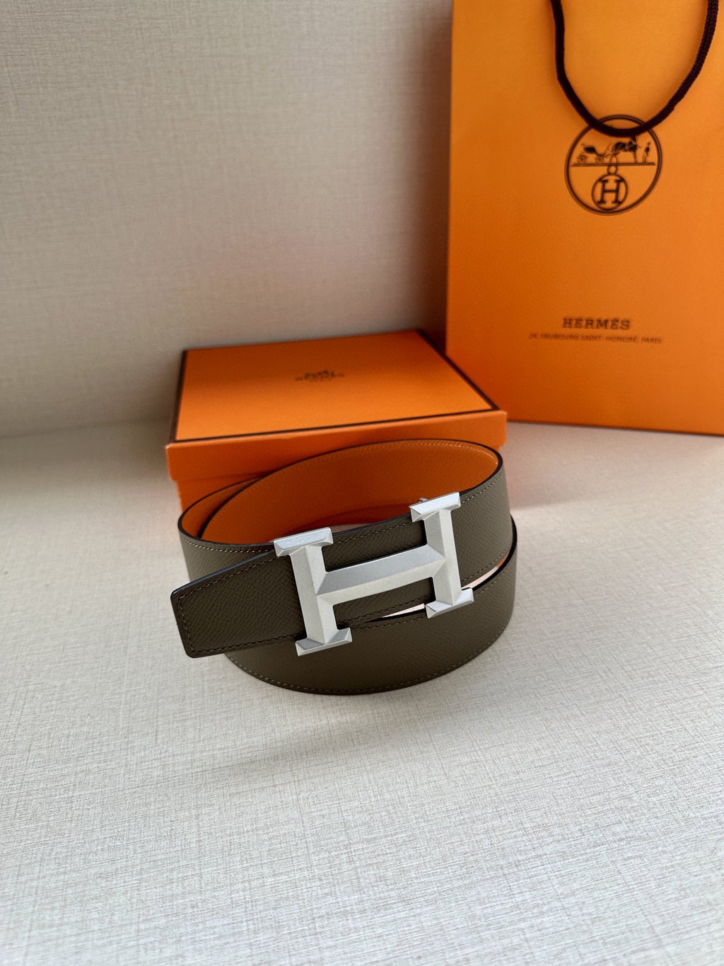 Hermes belt resting with dark strap and silver H buckle, single loop view