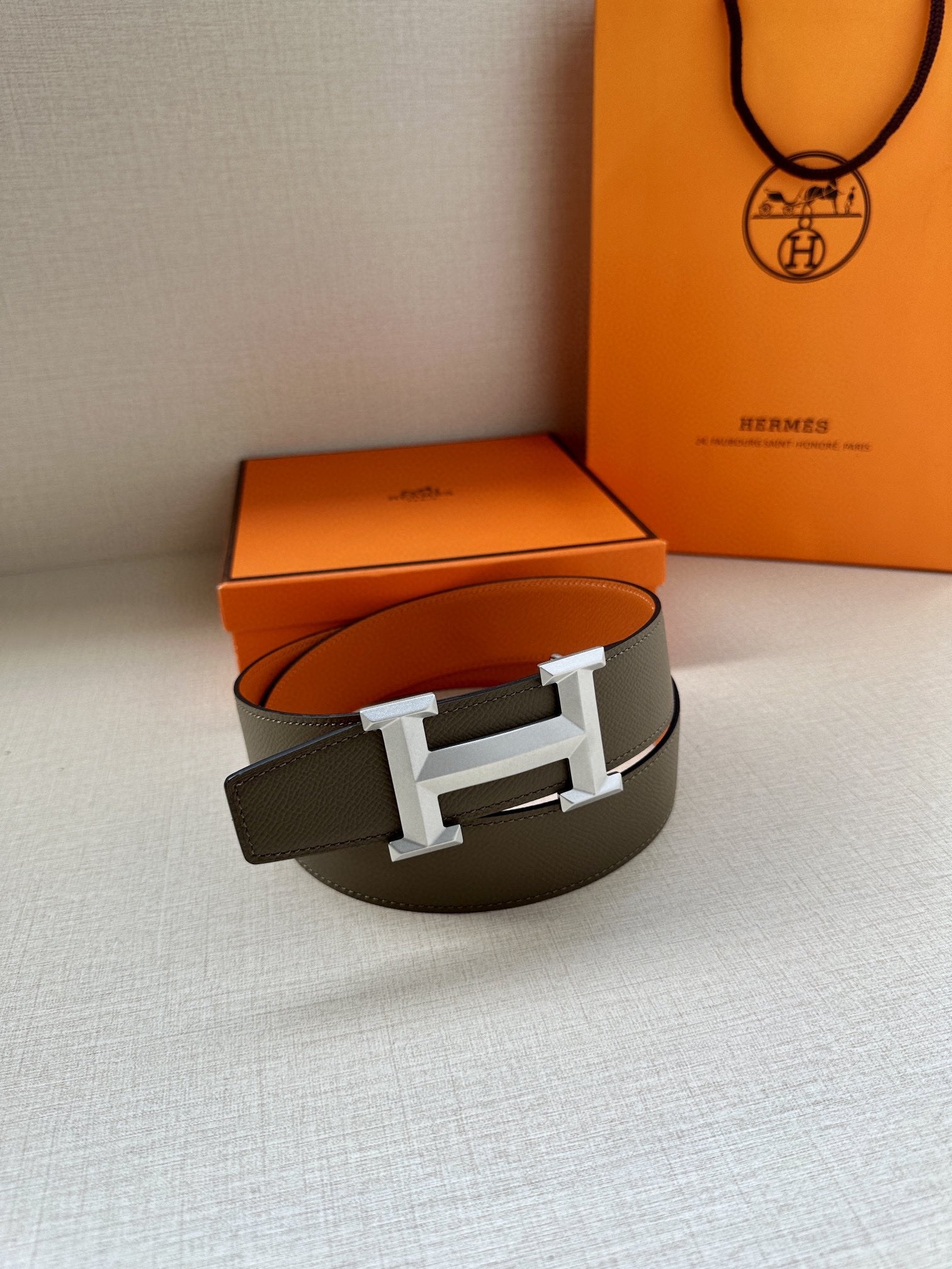 Hermes belt resting with dark strap and silver H buckle, single loop view