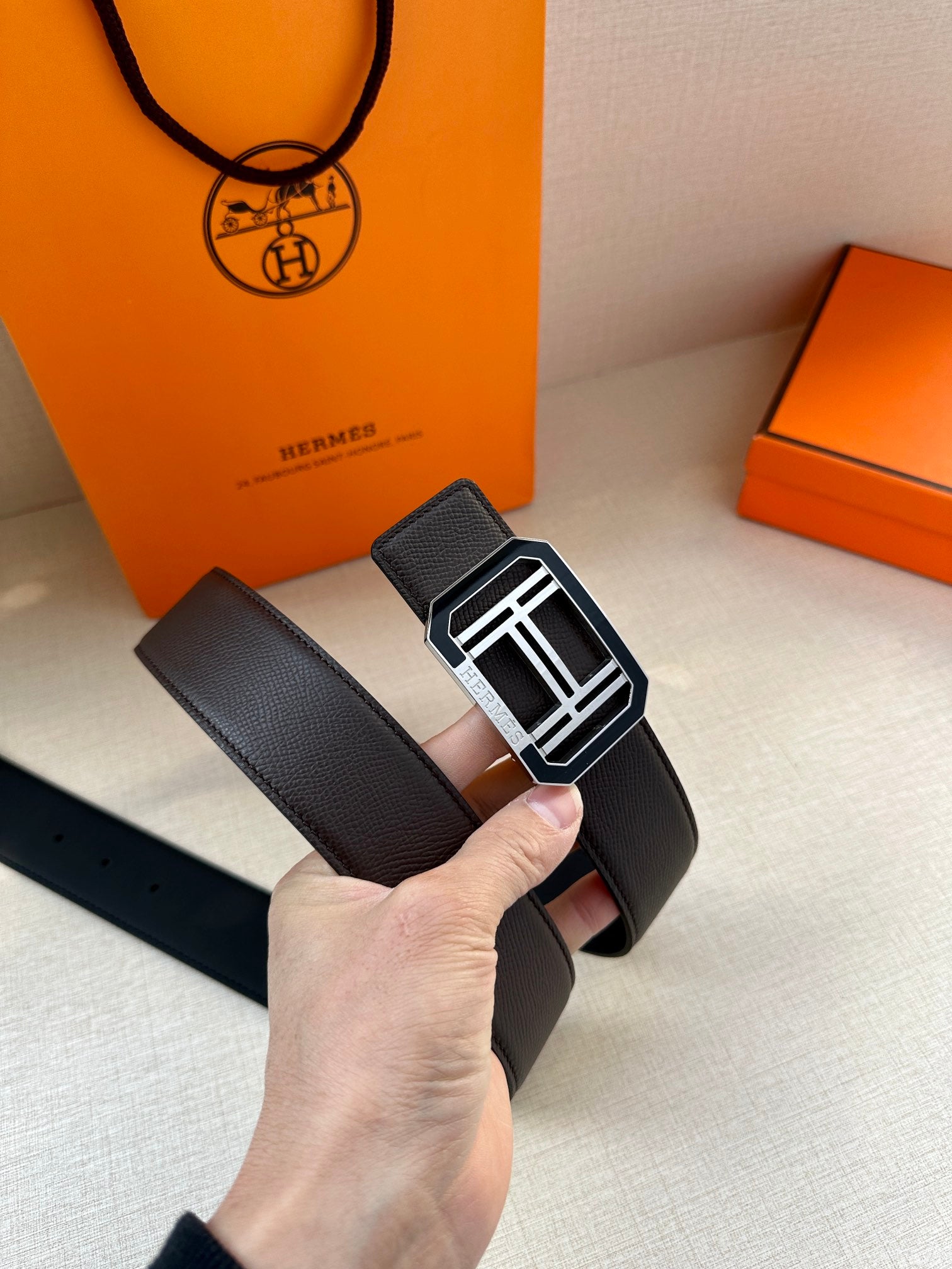 Dark leather belt with textured strap and silver square buckle, laid across hand