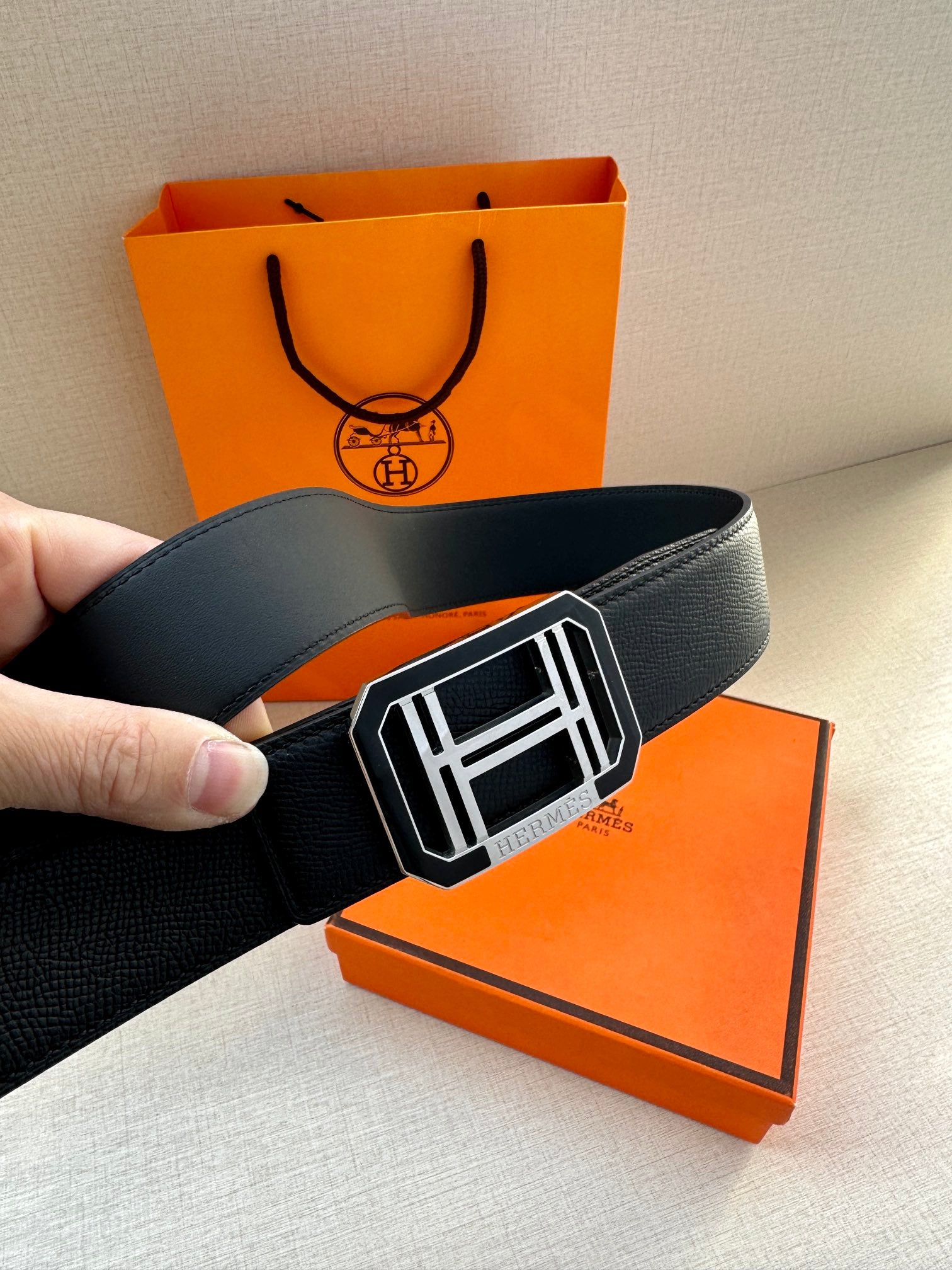 Hermes belt with dark leather strap and silver square buckle, laid across box