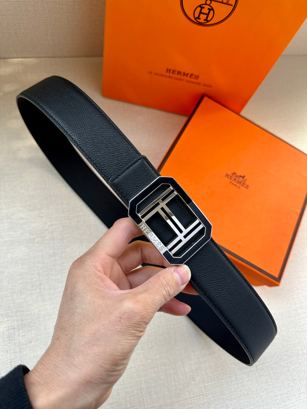 Hermes belt with dark leather strap and silver square buckle clasp, in hand