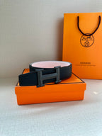 Leather belt with dark navy strap and gold H buckle, resting on box
