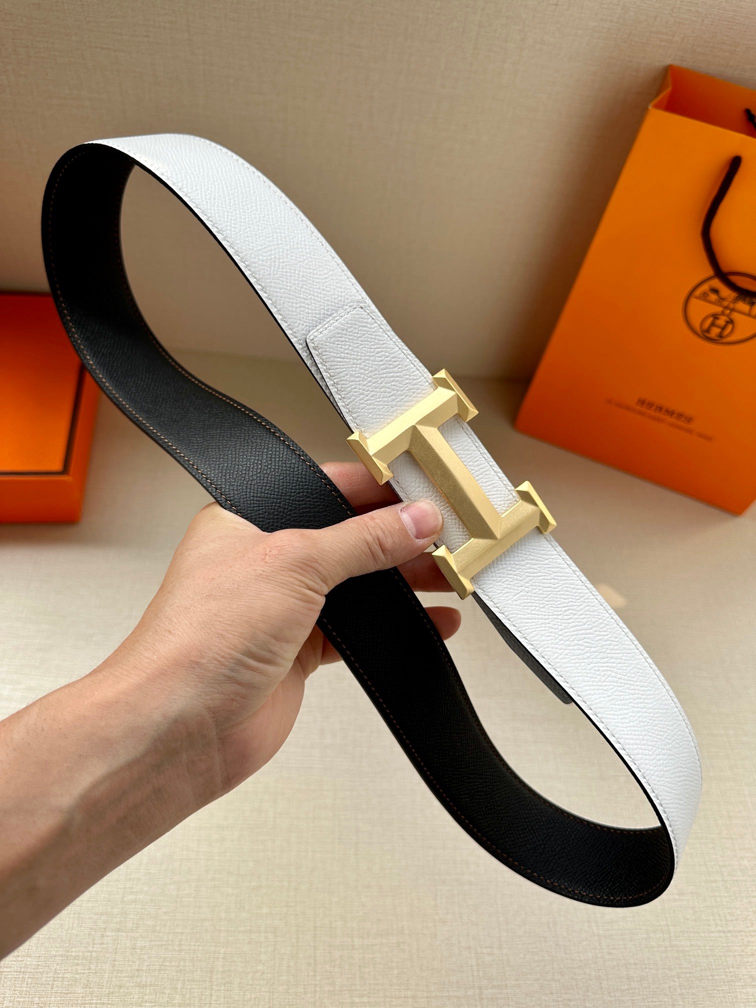 Leather belt with light gray strap and gold H buckle over black underside