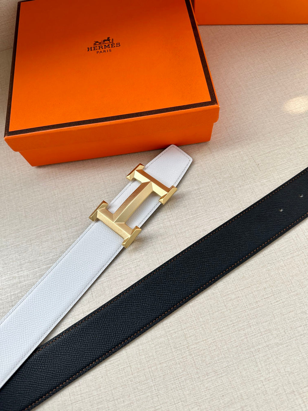 Two-tone leather belt with light gray and dark navy straps, gold H buckle