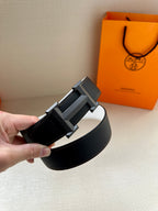 Leather belt with black strap and silver-tone H buckle, held at angle