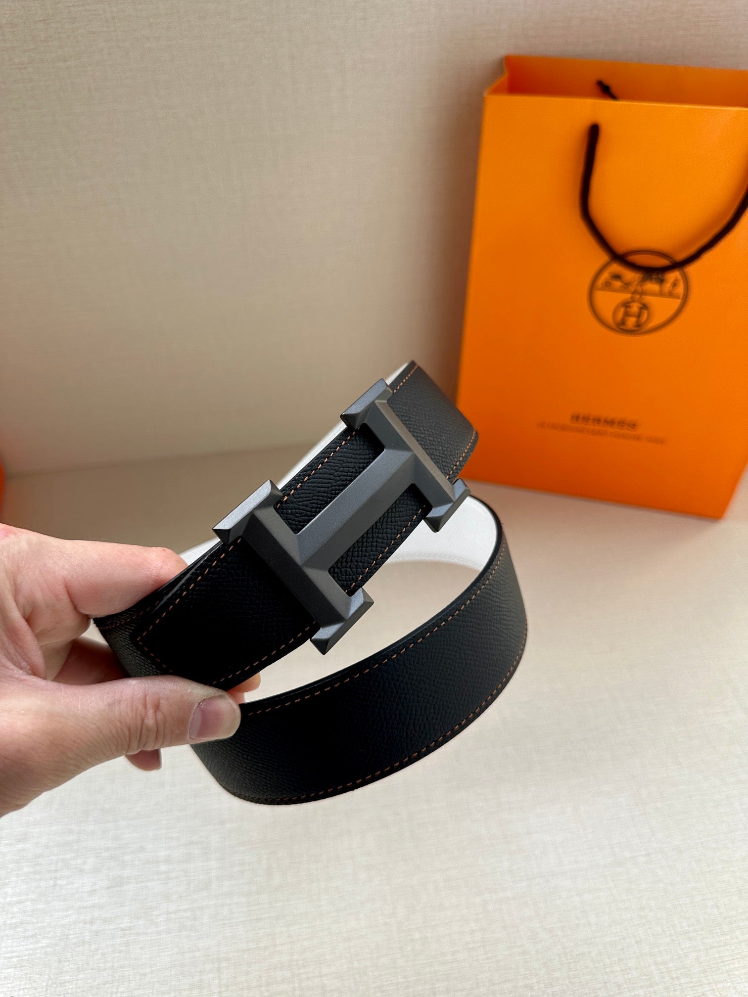 Leather belt with black strap and silver-tone H buckle, held at angle