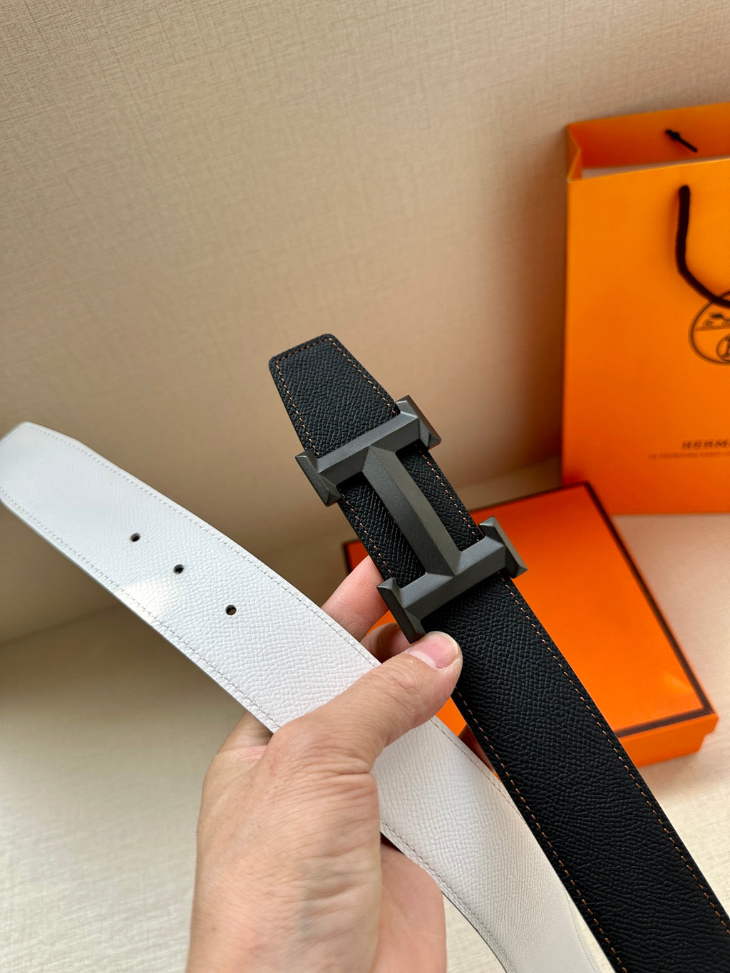Leather belt with white and black sides, silver-tone H buckle close-up