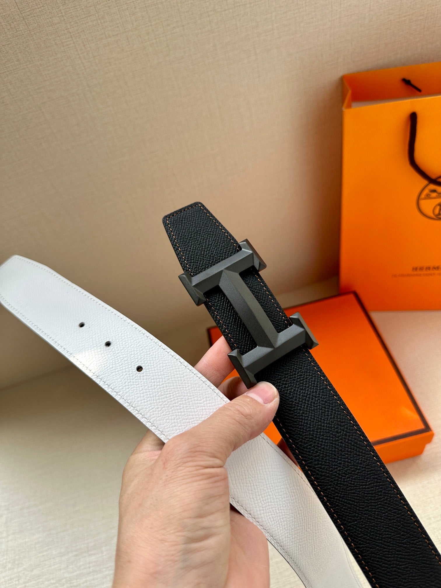 Leather belt with white and black sides, silver-tone H buckle close-up