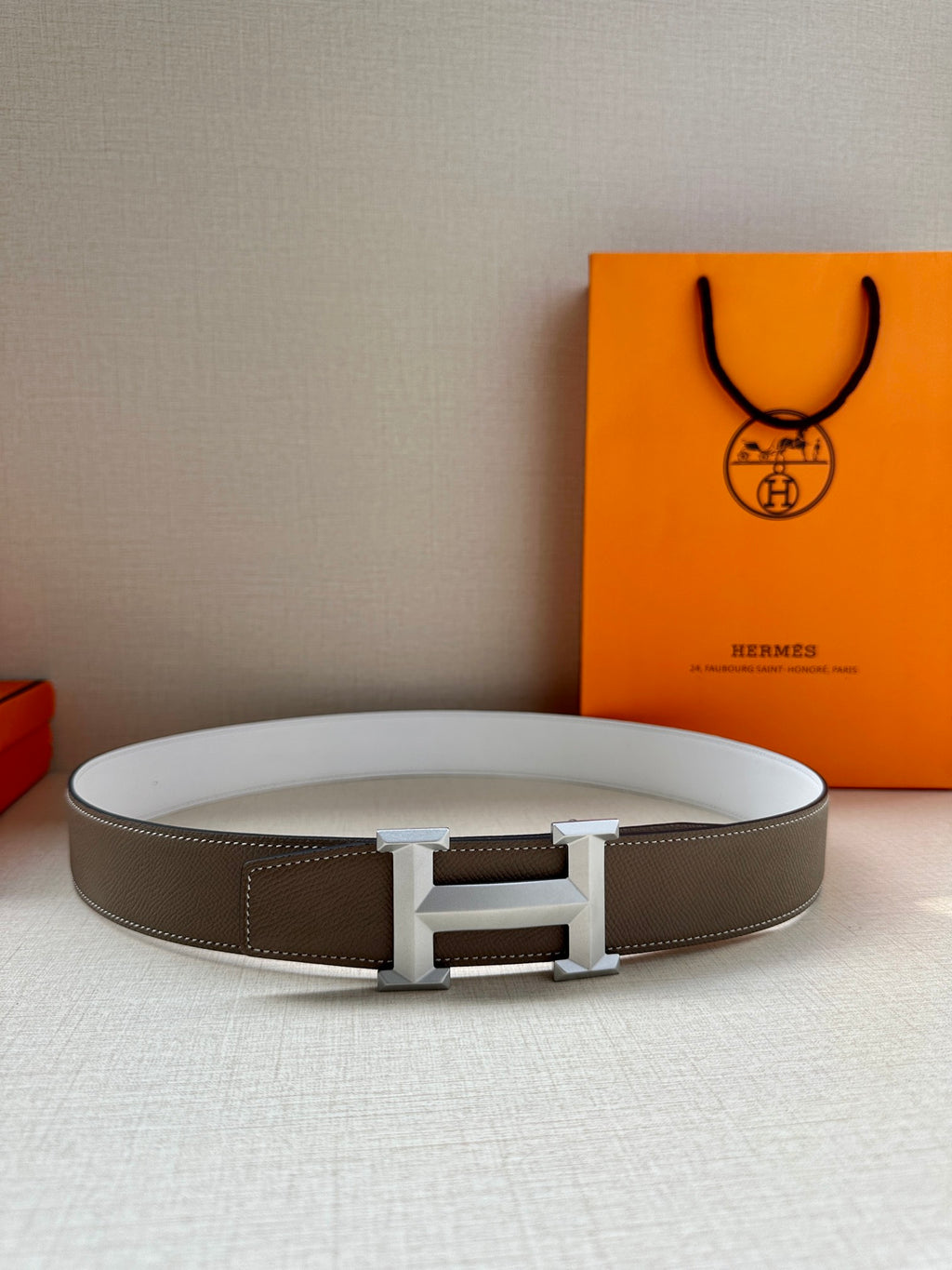 Hermes belt flat on surface: dark taupe leather strap with silver-tone center buckle