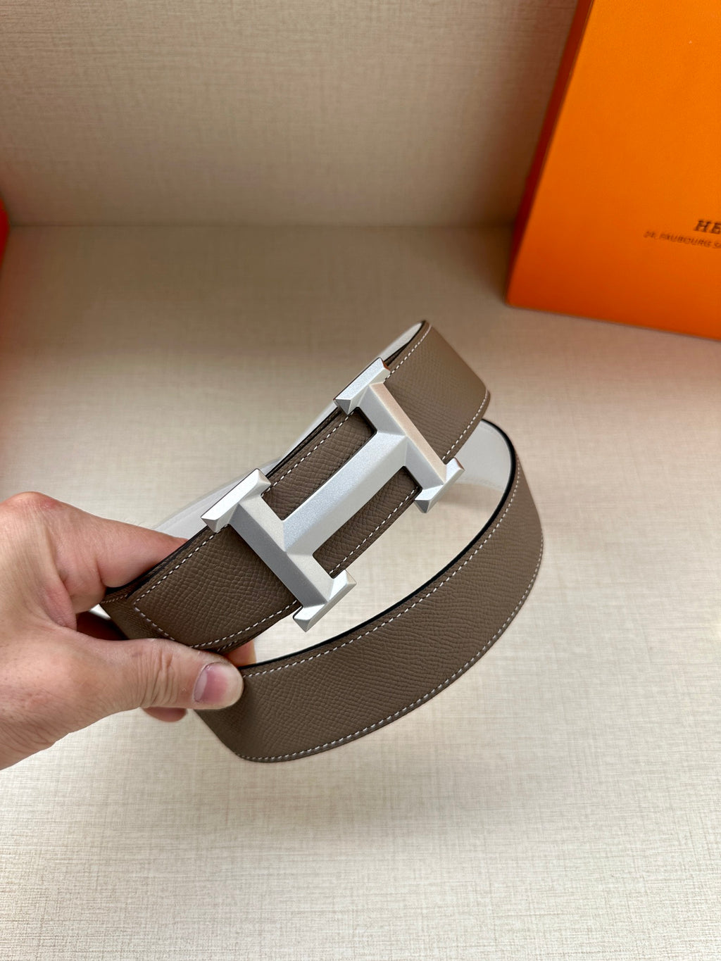 Hermes belt buckle close-up: dark taupe leather strap with silver-tone reversible buckle