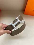 Hermes belt buckle close-up: dark taupe leather strap with silver-tone reversible buckle