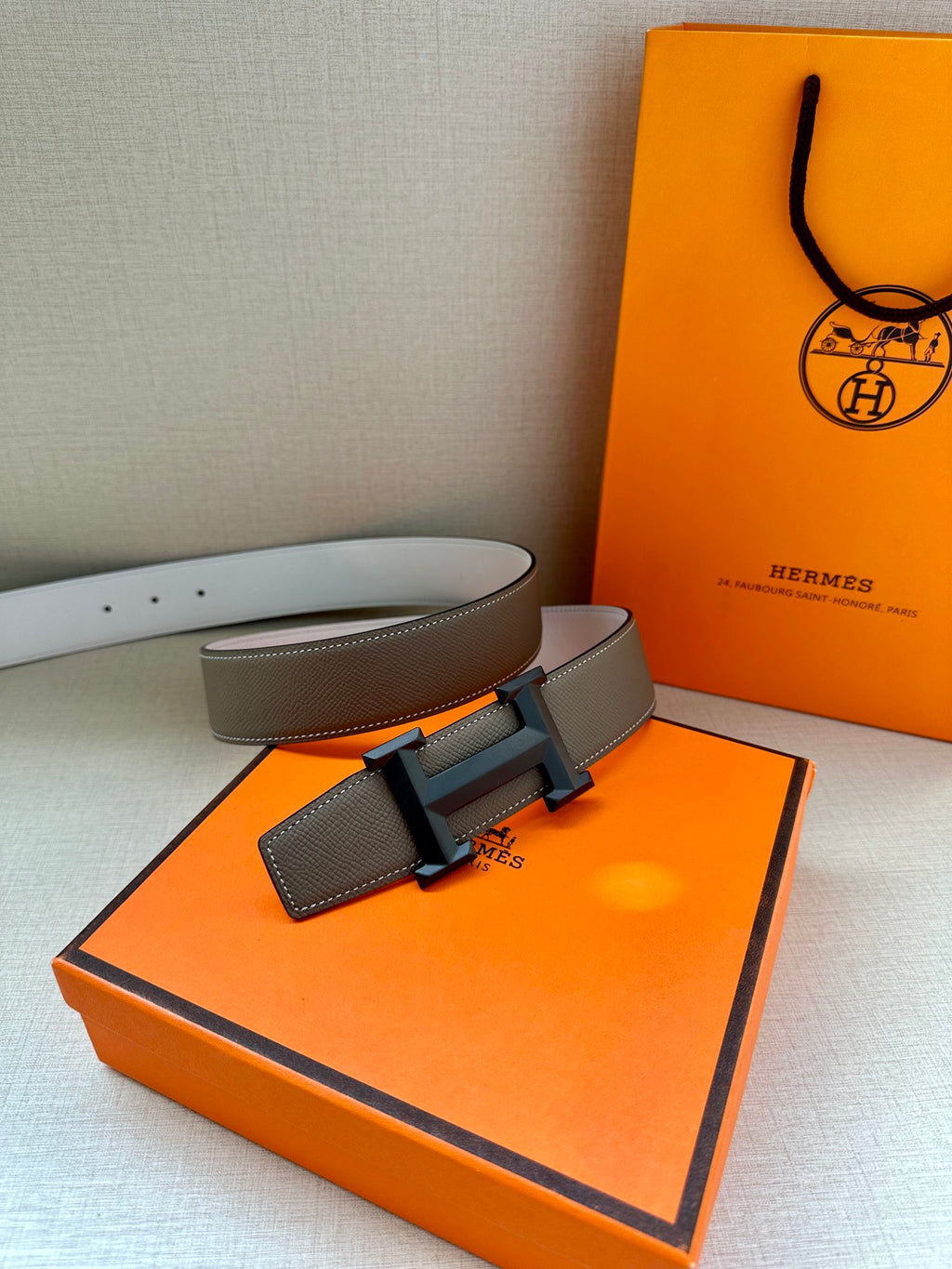 Hermes belt laid flat: taupe leather strap with black H buckle and leather keeper.