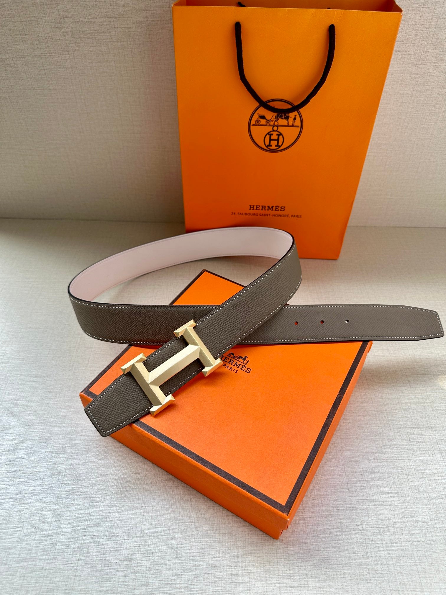 Hermes belt with dark taupe leather and light gold-tone reversible buckle on display