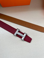 Hermes belt laid flat with burgundy strap, tan underside, and silver-tone buckle