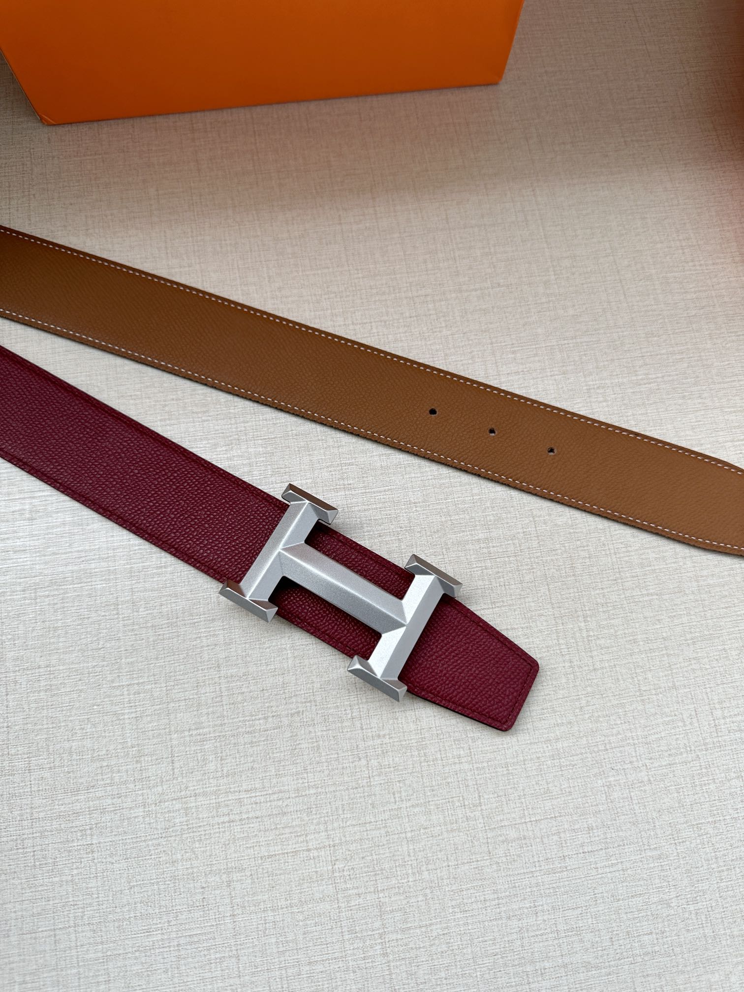 Hermes belt laid flat with burgundy strap, tan underside, and silver-tone buckle